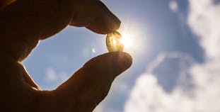 Vitamin D supplement held up in a hand with the sun shining behind it.