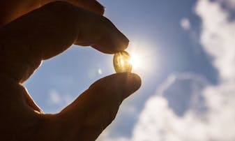 Vitamin D supplement held up in a hand with the sun shining behind it.