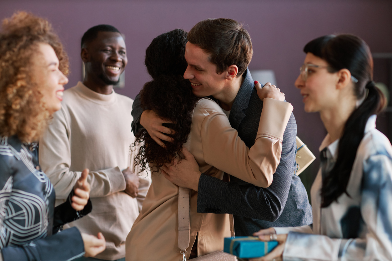 A man and woman hug while they are surrounded by friends.
