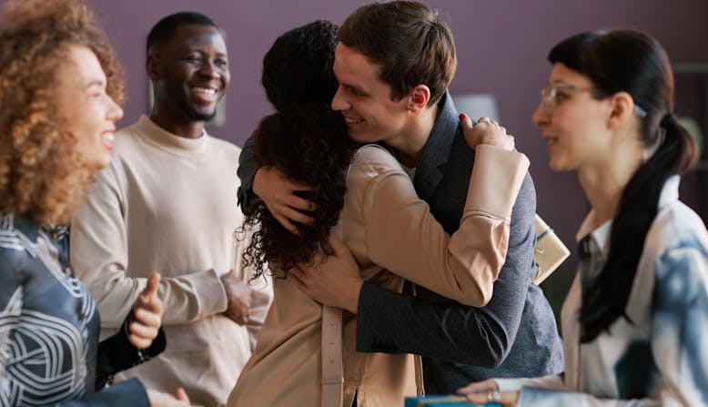 A man and woman hug while they are surrounded by friends.