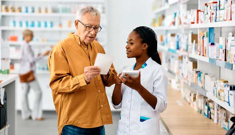 A woman pharmacist explains a medication label to a elderly man.