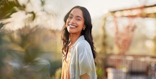 A woman smiling standing in the sun outside.