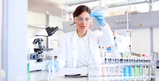 A woman scientific researcher sits in a lab and looks at a test tube with red liquid in it,