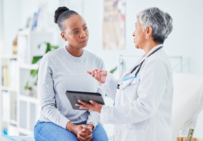A middle aged black woman talks with a doctor about related diseases.