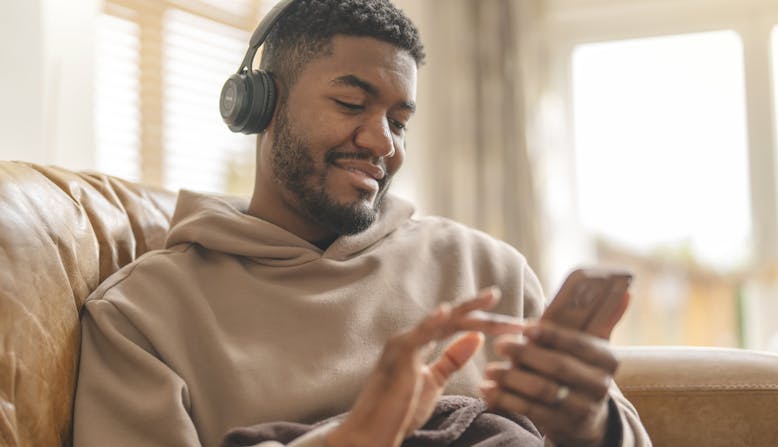 A Black man listens to a podcast with headphones.