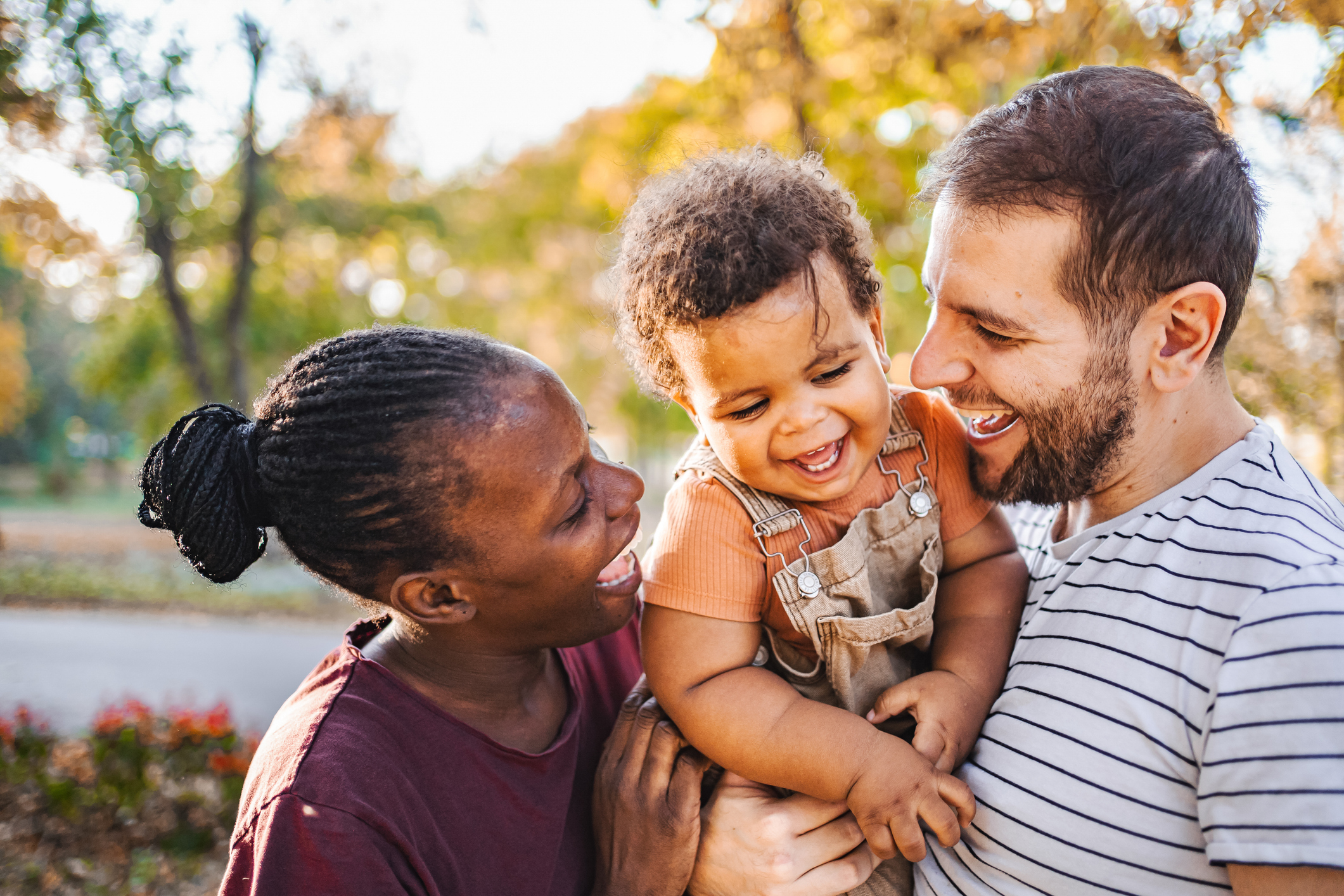 A family smiles together in a fall outdoor setting.