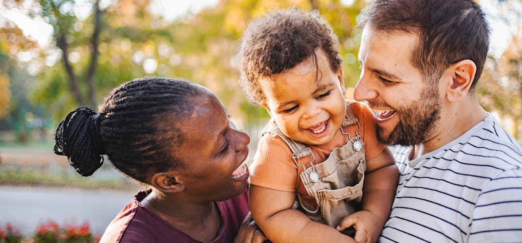 A family smiles together in a fall outdoor setting.