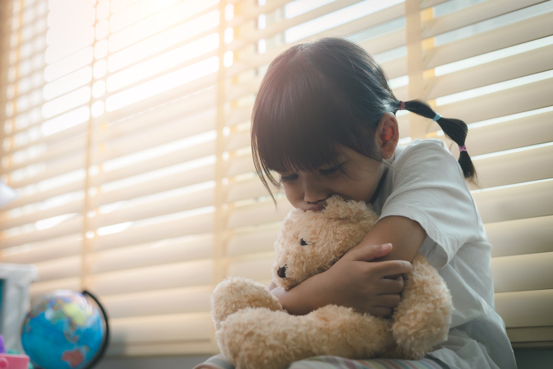A sad child deals with emotions while hugging a teddy bear. 