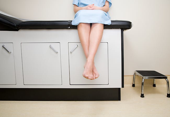 A woman waits on an examination table at a doctor's office, while wearing a blue examination gown.