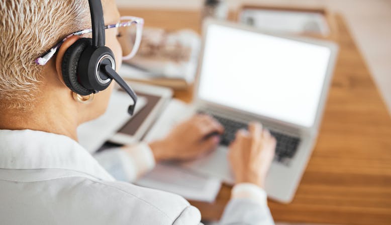 A woman wears a headset while answering an email on her laptop.