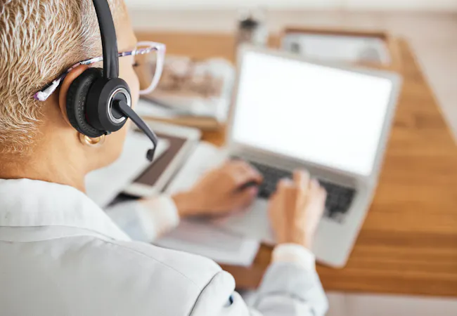 A woman wears a headset while answering an email on her laptop.