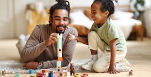 A father and daughter play with blocks in the living room.