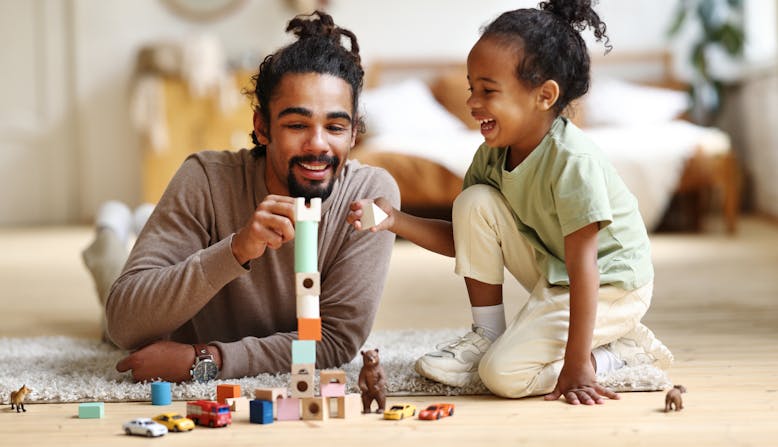 A father and daughter play with blocks in the living room.