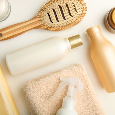 Several bottles of shampoo and conditioner laying down with a towel and a hair brush.