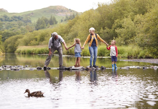 A family crosses water over stones while holding hands.