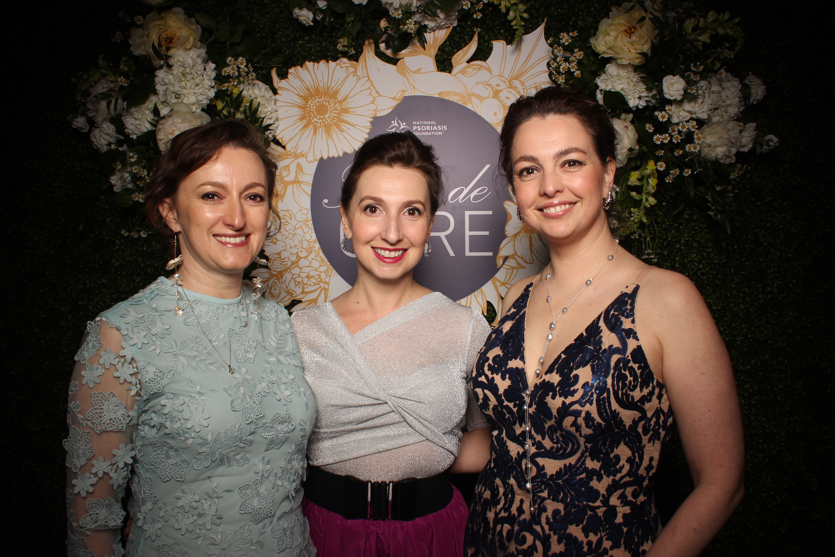 Three women stand in front of the NPF Fleur de Cure sign.