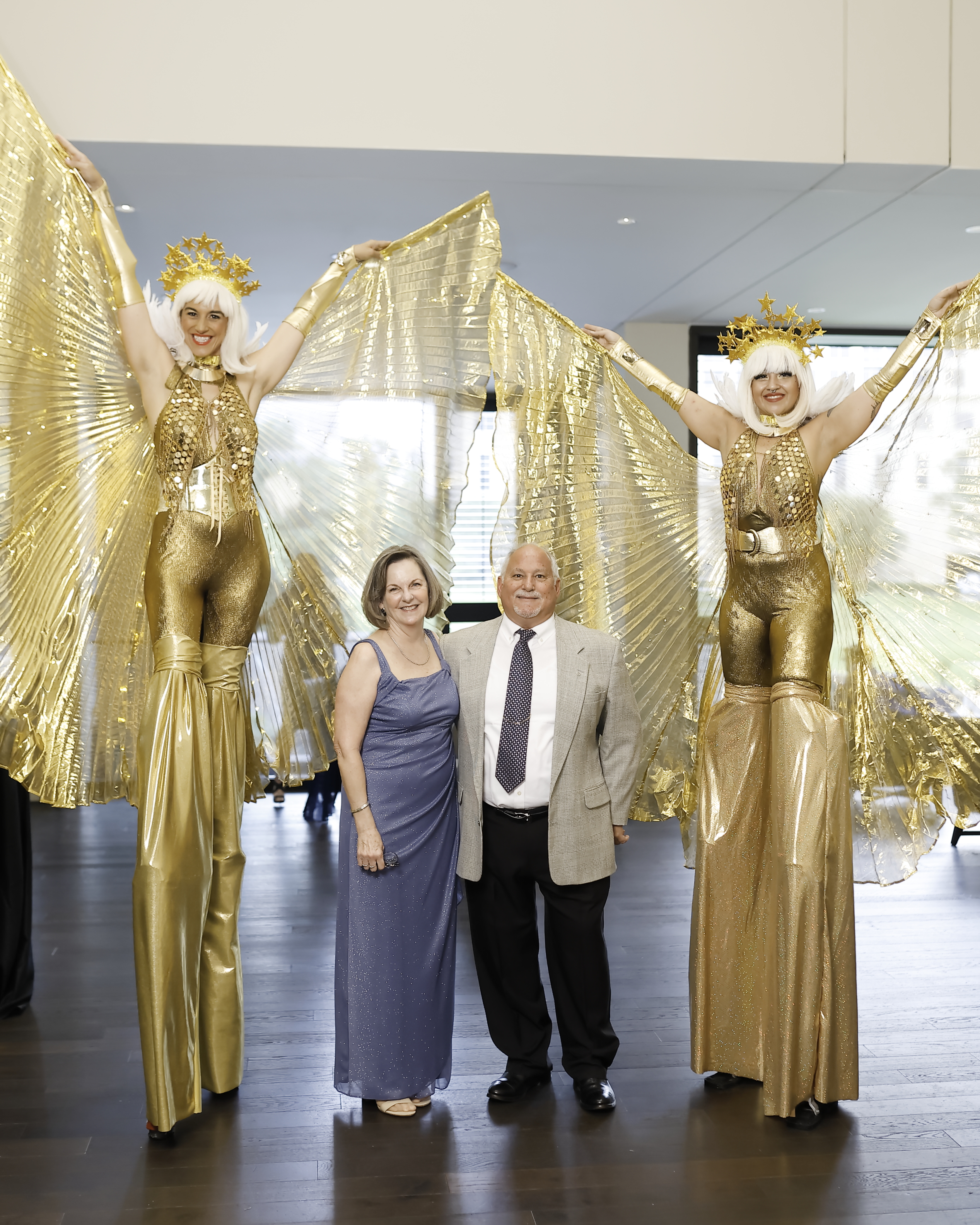 Two attendees of the Houston Starlight Soiree pose with women on stilts.