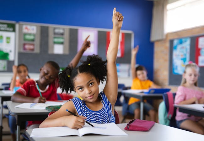 A classroom of kids raising their hands.