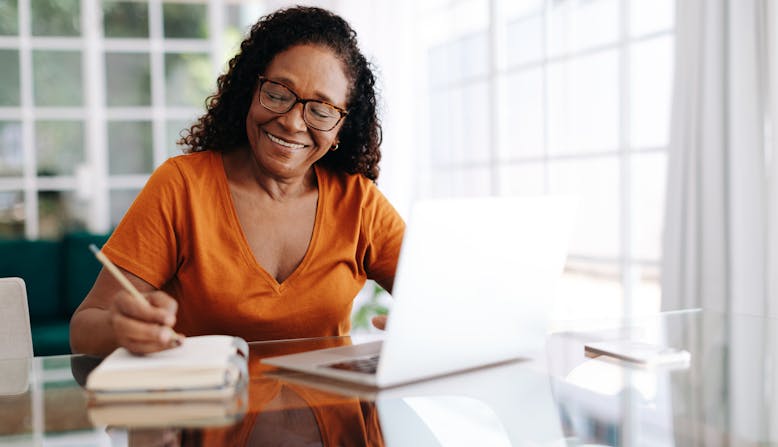 An older black woman looks at her computer and takes notes.