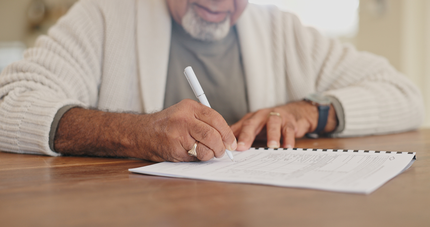 An older man sits at a table and works on a paper checklist.
