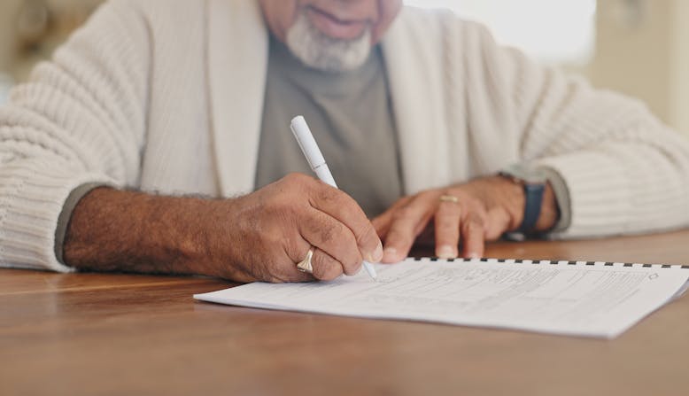 An older man sits at a table and works on a paper checklist.