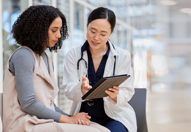 A patient and doctor look at a clipboard in a hallway.