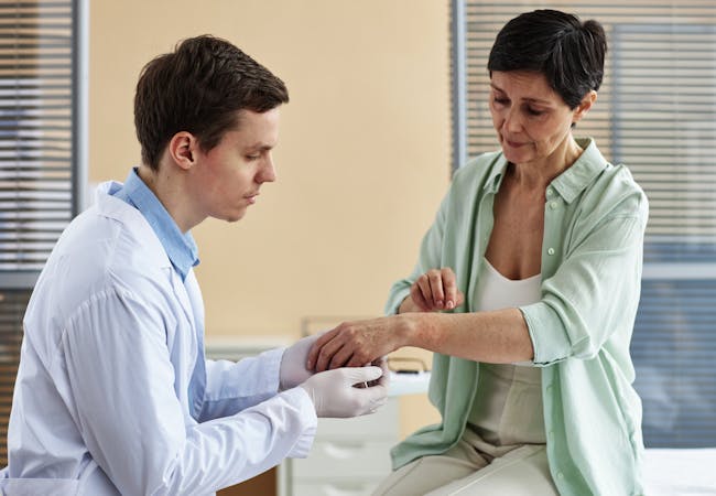 A doctor looks at a patient's skin on her arm.