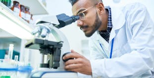 A researcher looks through a microscope in a lab.