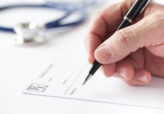 A hand holding a pen hovers over a prescription paper.