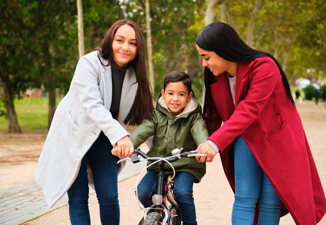 Latine lesbian couple teaching their child to ride a bike.