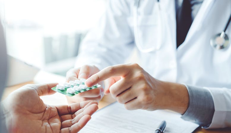 A doctor hands over a packet of pills while explaining to patient.