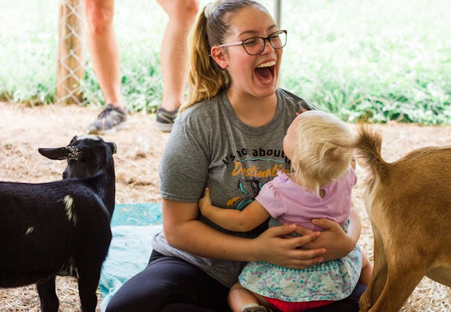 A mom and infant daughter enjoy a goat petting zoo.