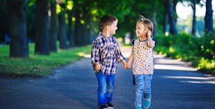 Two young children smiling and holding hands on a path.