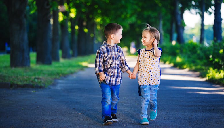Two young children smiling and holding hands on a path.