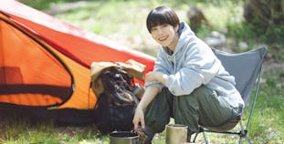 An Asian woman with short hair cooks dinner while camping.