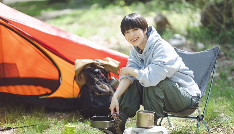 An Asian woman with short hair cooks dinner while camping.