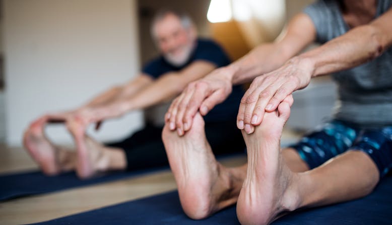 Two older individuals holding their feet while stretching.