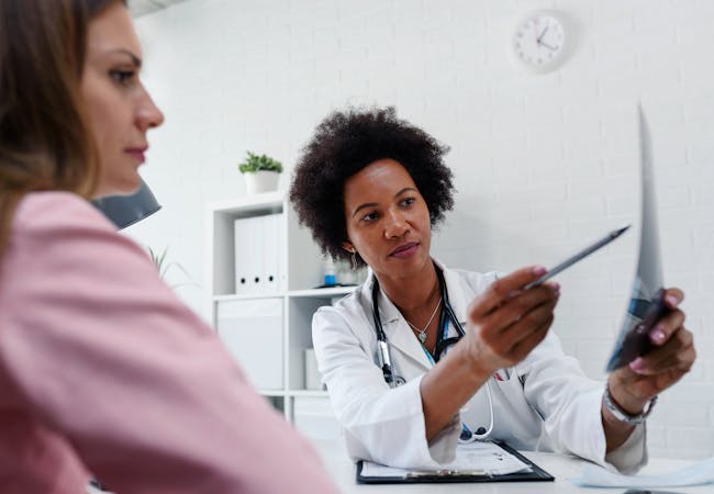 A female doctor points something out to her female patient on a piece of paper. 