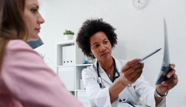 A female doctor points something out to her female patient on a piece of paper.