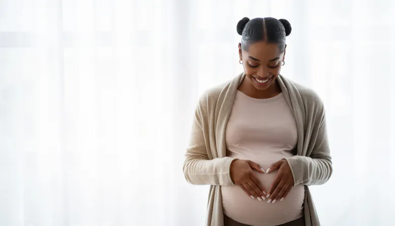 A Black pregnant woman holds her hands on her belly.