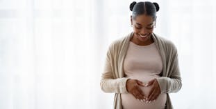 A Black pregnant woman holds her hands on her belly.