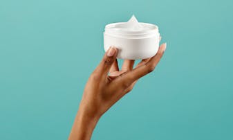 A hand holding a skin lotion jar.