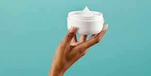 A hand holding a skin lotion jar.