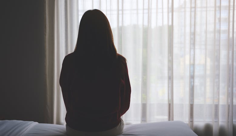 Woman sitting on a bed looking out the window.