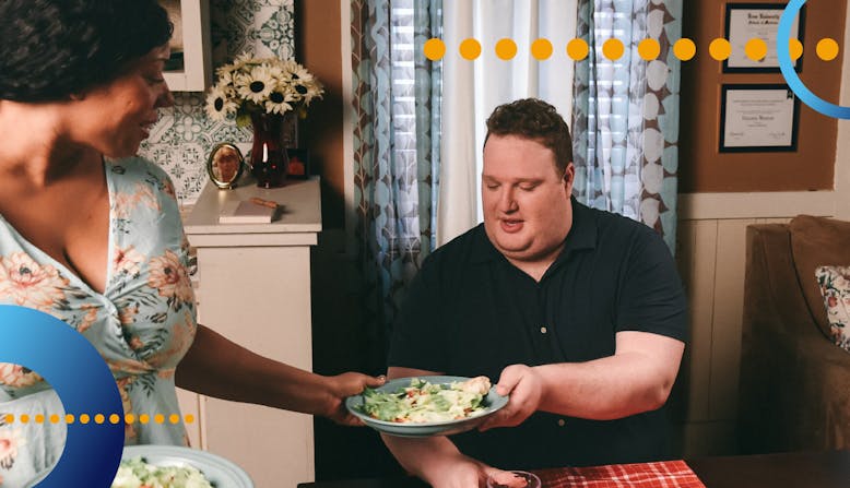 A woman hands a man who is sitting at a table food.