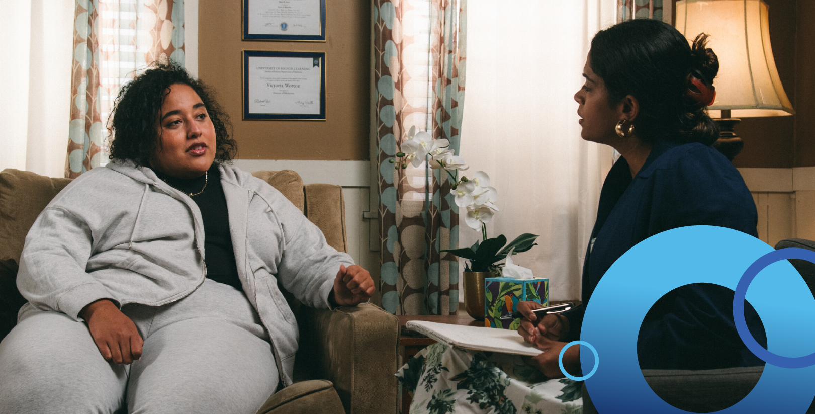 Two women sitting and talking, one holds a clipboard.