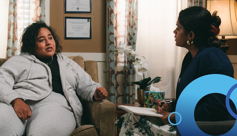 Two women sitting and talking, one holds a clipboard.