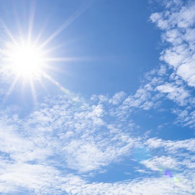 Bright sun in a blue sky with clouds.