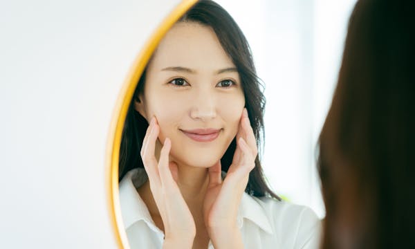 A woman looks in the mirror smiling and touching her face.