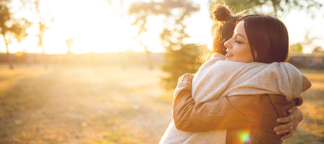 Two women embracing with a sunset behind them.